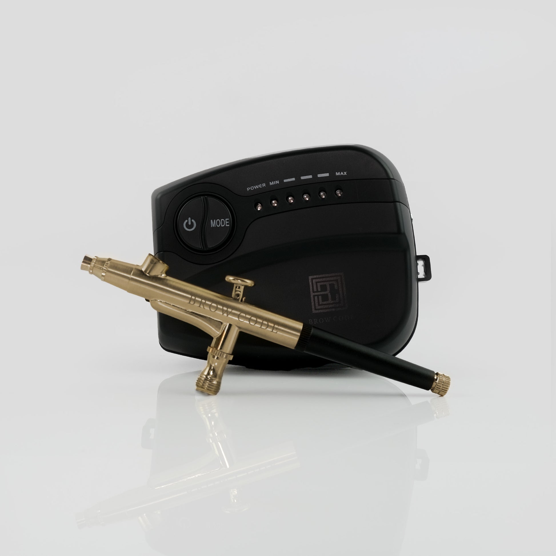 Eine schwarze Brow Code Airbrush Maschine AirArchist mit einem goldenen und schwarzen Werkzeug, dargestellt auf einem weißen Hintergrund. Blashy Shop