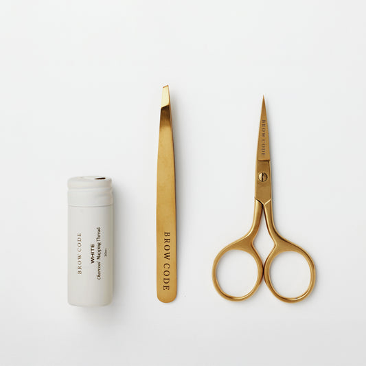 Das Brow Code AT HOME KIT Brow Mapping & Styling besteht aus einer weißen Tube, einer goldenen Pinzette und einer goldenen Schere. Blashy Shop