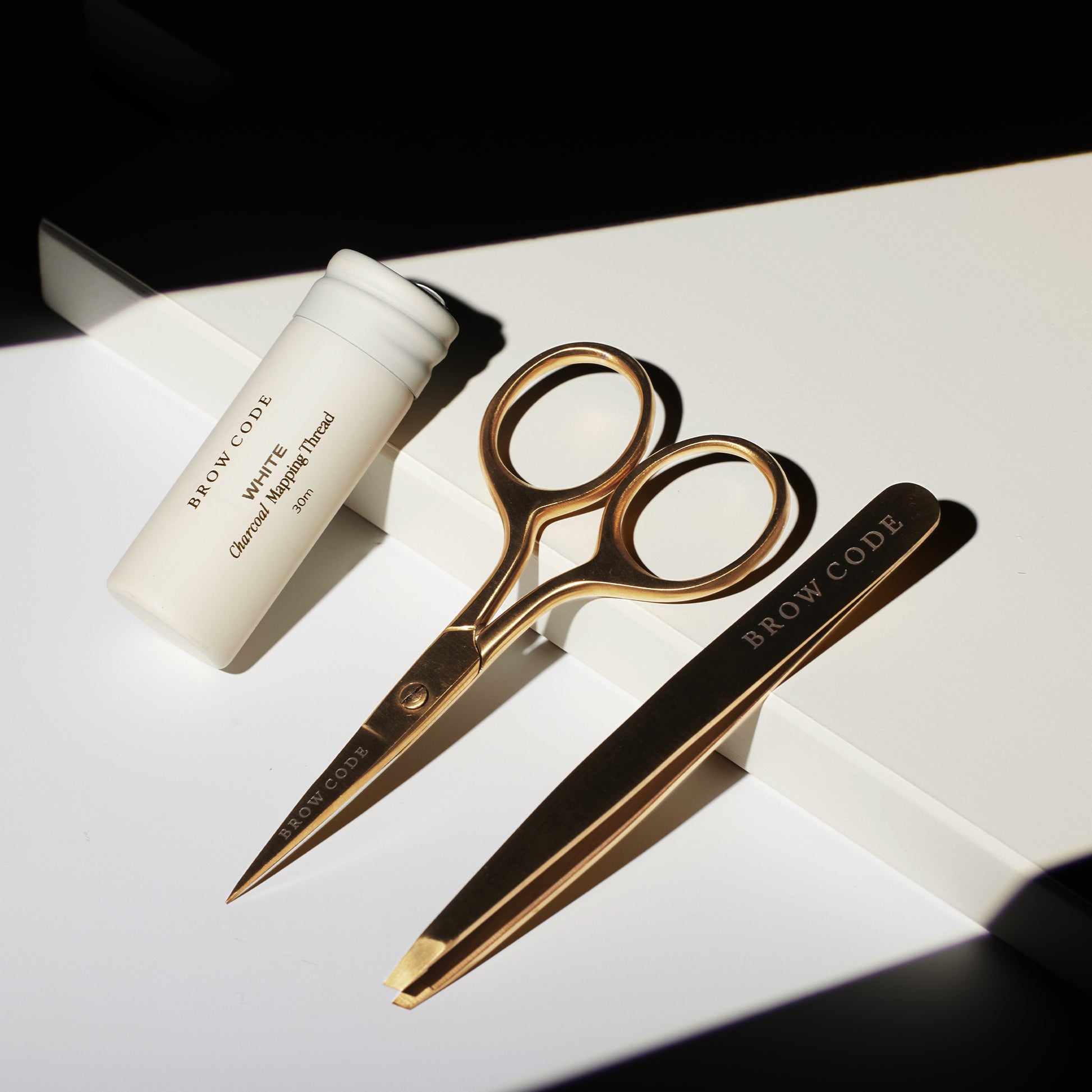 Das Brow Code AT HOME KIT Brow Mapping & Styling, mit goldener Schere und Pinzette, ruht auf einer weißen Unterlage. Blashy Shop