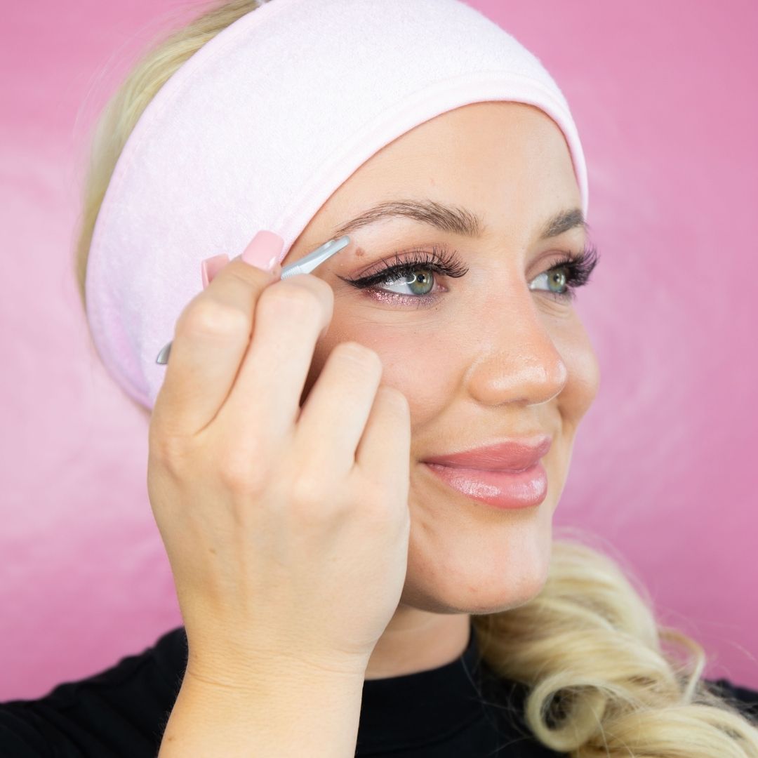 Frau mit rosa Stirnband benutzt die Blashy EASY TWEEZY Augenbrauen-Pinzette - rund vor rosa Hintergrund. Blashy Shop
