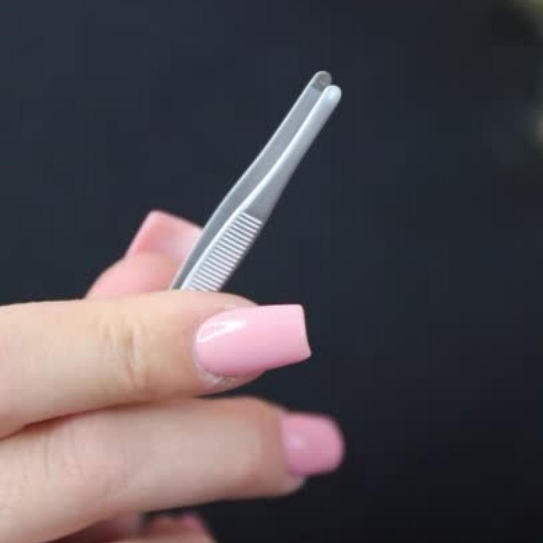 Eine Hand mit rosa Nägeln hält eine BLASHY EASY TWEEZY Augenbrauen-Pinzette - rund von Blashy vor einem dunklen Hintergrund. Blashy Shop
