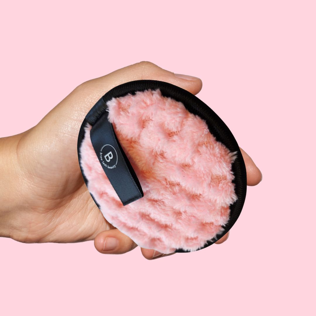 Eine Hand hält ein rosa, rundes BLASHY FLAUSCHY Abschminkpad von Blashy-soft, mit schwarzem Rand und Stoffanhänger. Blashy Shop