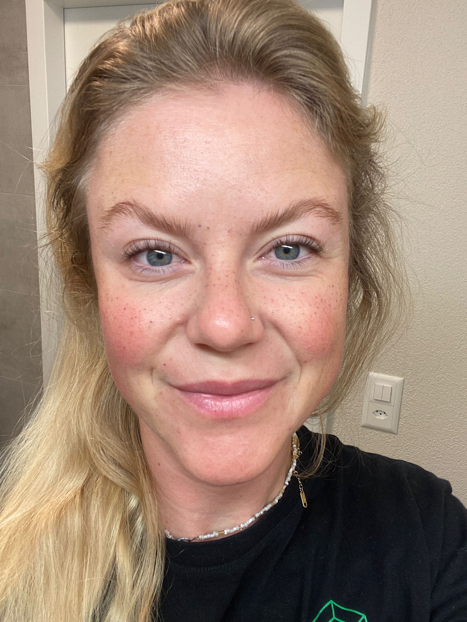 Eine blonde Frau mit heller Haut lächelt nach der Anwendung von Blashy LIFTY One Step Lash & Brow Lamination - 5ml in Innenräumen. Blashy Shop
