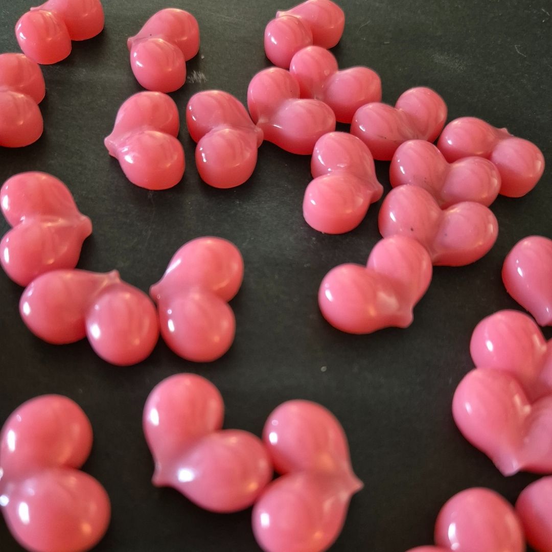 Kleine, rosafarbene, herzförmige BLASHY Waxy Wax Pellets (Rose, 300g) sind auf einer dunklen Oberfläche verstreut. Blashy Shop