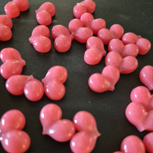 Kleine, rosafarbene, herzförmige BLASHY Waxy Wax Pellets (Rose, 300g) sind auf einer dunklen Oberfläche verstreut. Blashy Shop