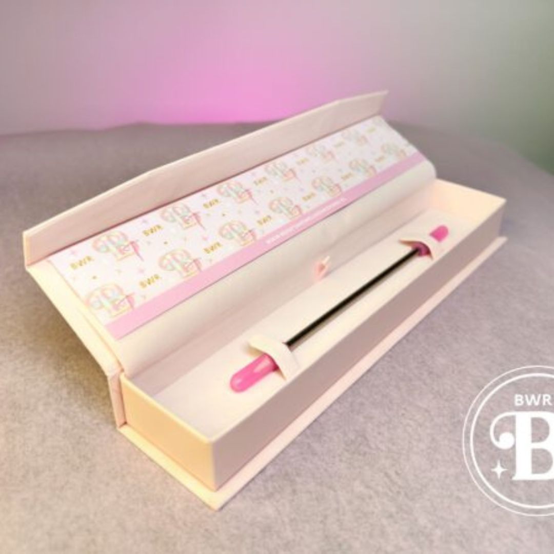 Ein rosafarbenes und silbernes BWR Brow Tool von blashyshop.com in einer offenen weißen Box mit einem gemusterten Inneren auf einer grauen Oberfläche. Blashy Shop