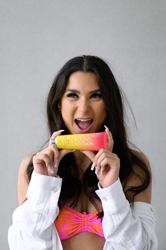 Frau im rosa Bikini-Oberteil lächelt und hält FOUND MY SKIN SPF 8 Melanin Boost Feuchtigkeitscreme. Blashy Shop