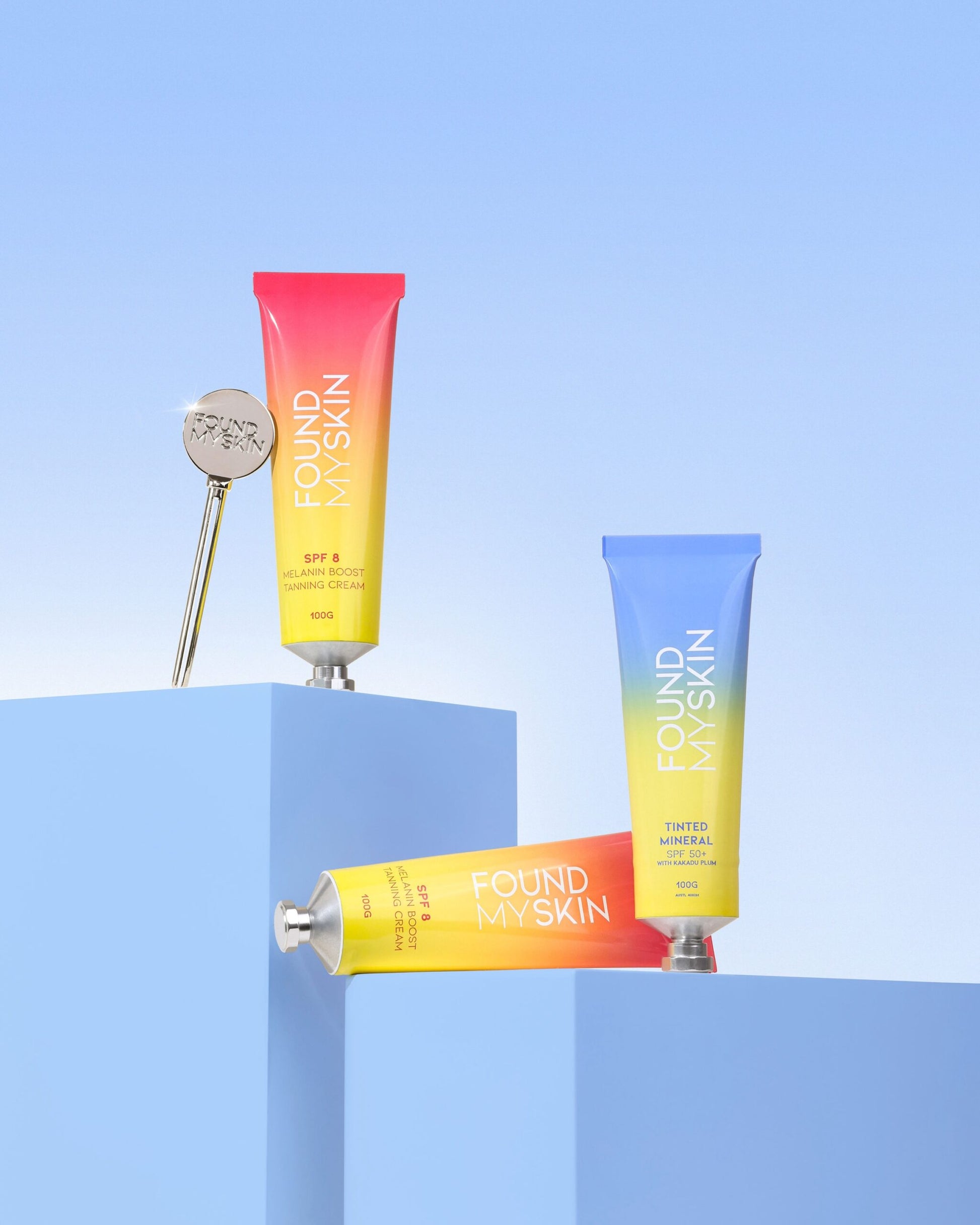 Drei FOUND MY SKIN SPF 8 Melanin Boost Feuchtigkeitscreme Tuben auf blauen geometrischen Podesten. Blashy Shop