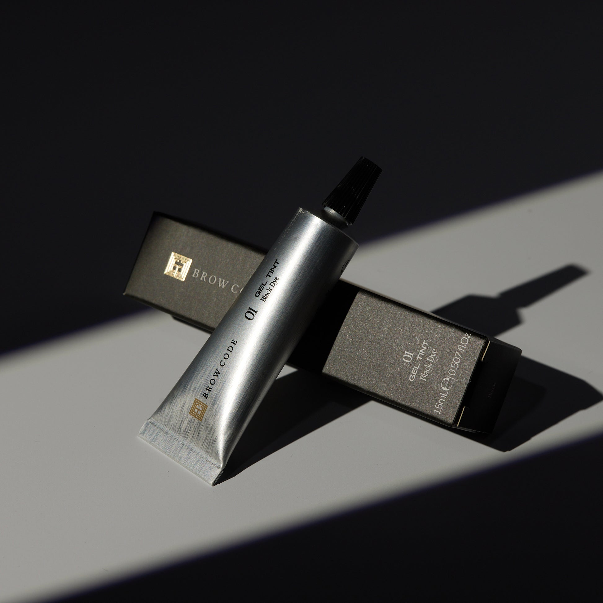 Eine silberne Tube Brow Code Gel Augenbrauenfarbe - natürlich & sensitiv, PPD frei, 15ml ruht auf ihrer Schachtel im Sonnenlicht. Blashy Shop