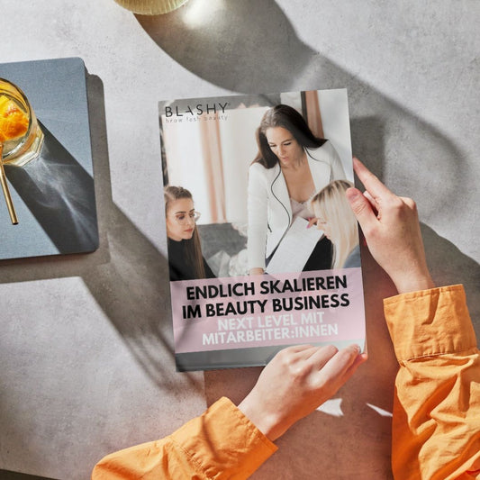 Person hält das Gratis EBook Endlich Skalieren im Beauty Business von Lash&Brow Academy Online - Next Level mit Team. Blashy Shop