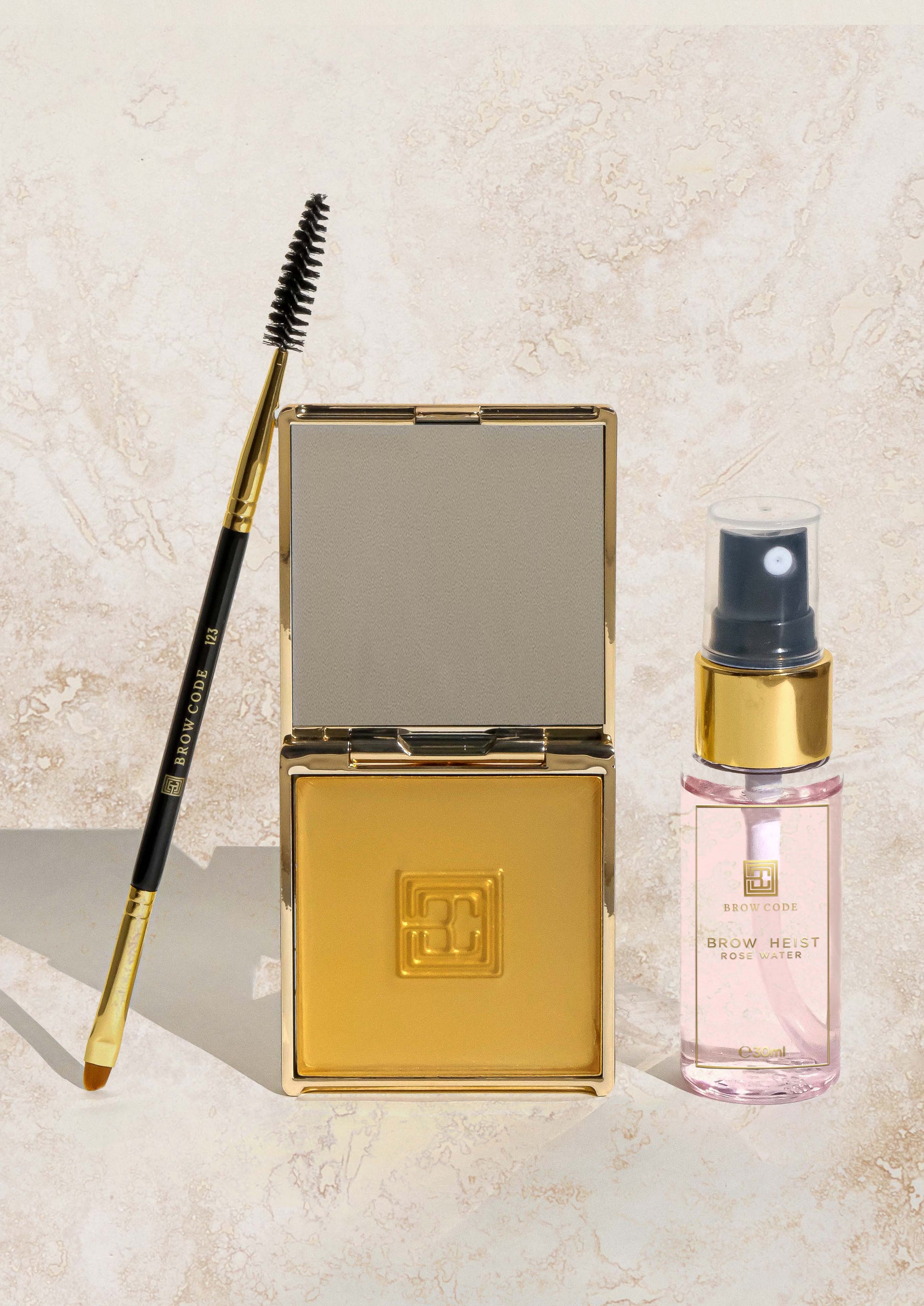 Ein Augenbrauenpinsel, Brow Soap aktivierend, und Brow Code Rosenwasser Spray, 30ml auf einer hellen Steinoberfläche. Blashy Shop
