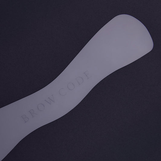 Ein Brow Code Spatel neben dem Silikonpad für Brow Lamination & Aufhellung auf dunklem Hintergrund. Blashy Shop