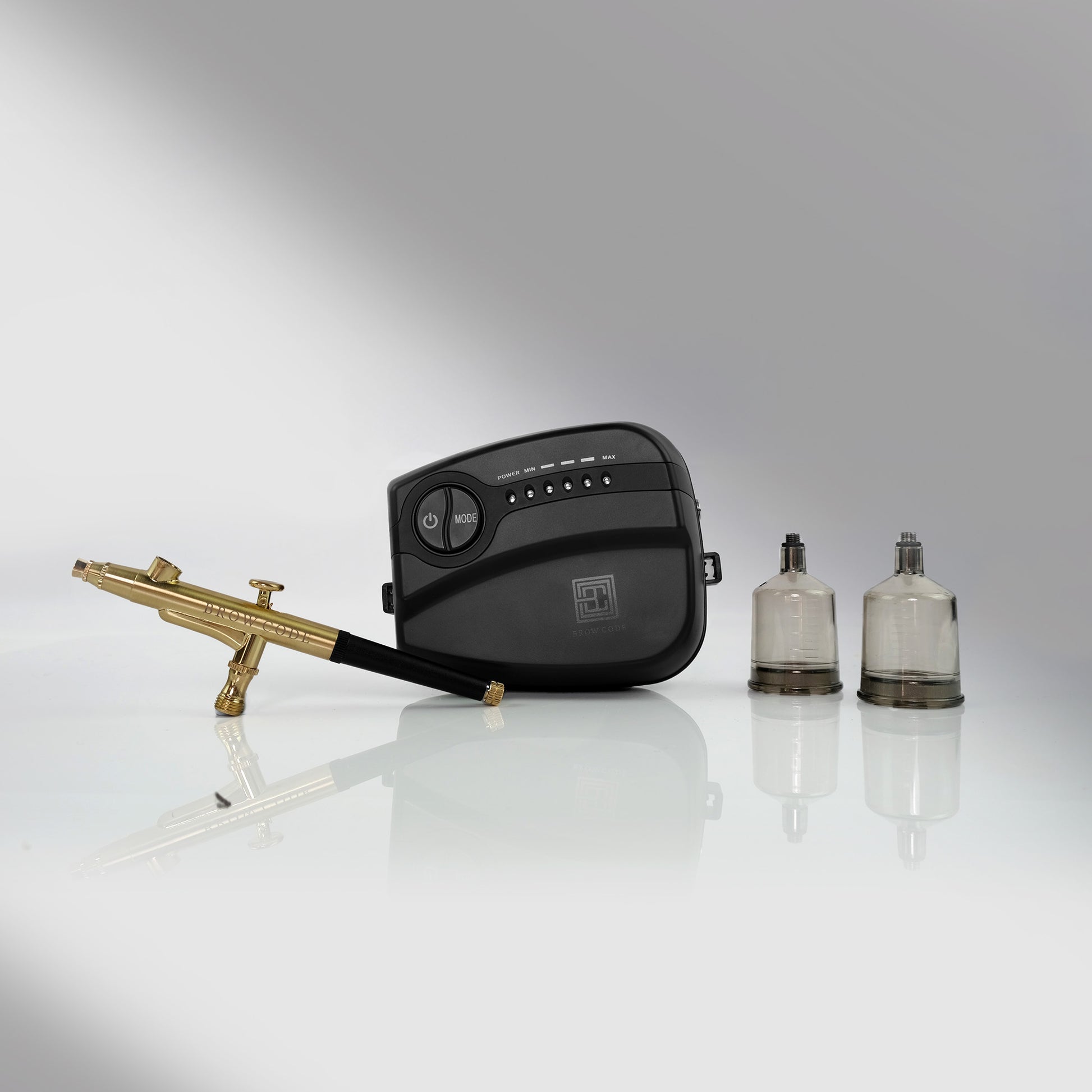 A Brow Code STARTER KIT Airbrush mit 10 Hybridfarben, Airbrush-Maschine und Zubehör auf einer reflektierenden Oberfläche. Blashy Shop